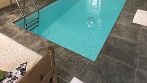 A rectangular indoor swimming pool with clear blue water, surrounded by stone tiles and equipped with metal ladders.