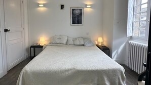 A bedroom with a large bed, two bedside tables with lamps, a framed picture on the wall, and a window with blinds.