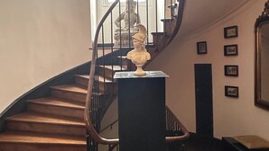 A grand staircase with a curved design, a statue on the landing, and framed pictures on the wall.