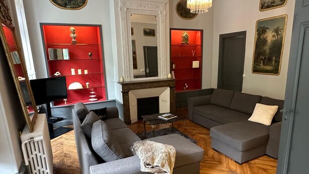 A living room with a fireplace, two grey sofas, a small table, and a red accent wall with shelves.