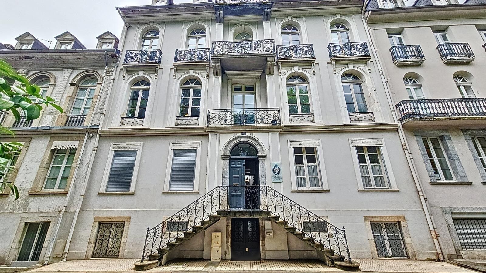 A multi-story building with a central entrance, a staircase leading to the entrance, and balconies with ornate railings.