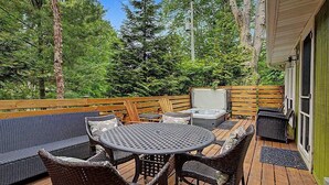 Una terraza de madera con mobiliario exterior, que incluye una mesa redonda y sillas de mimbre, además de un jacuzzi.