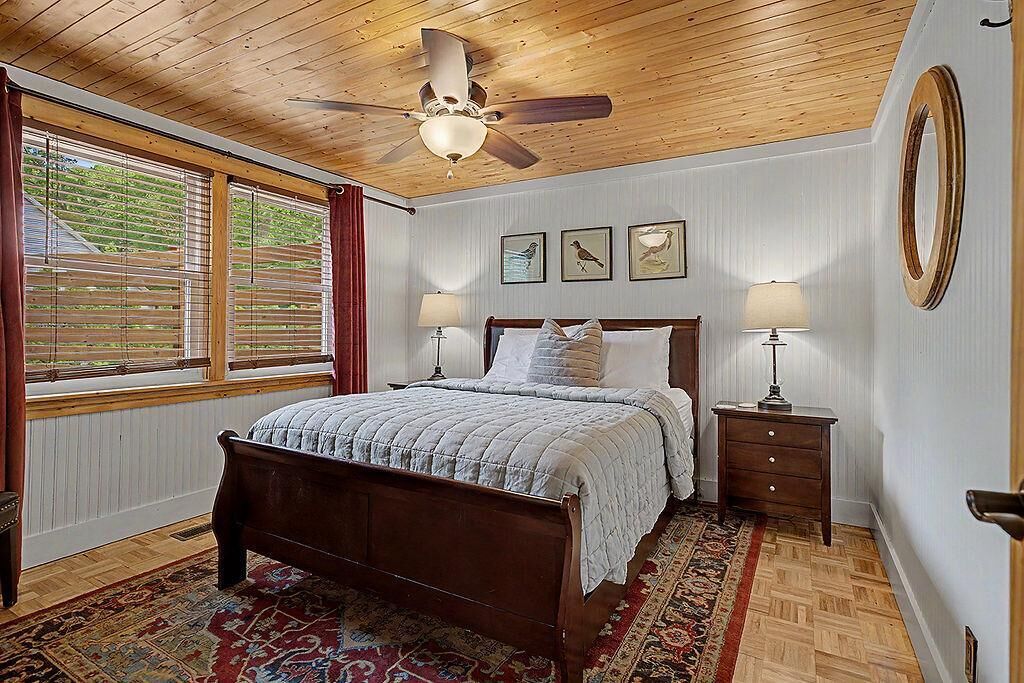Een slaapkamer met een houten plafond, een bed met een sprei, twee nachtkastjes met lampen, en een raam met zonwering.
