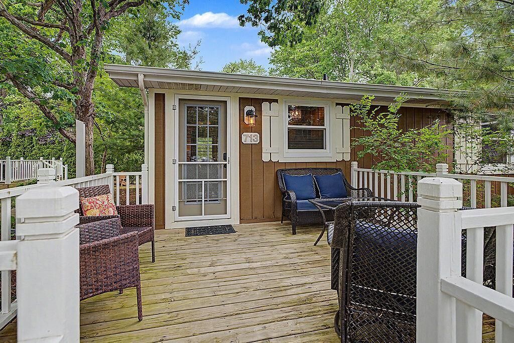 A wooden deck with wicker furniture, a door, and a window with shutters.