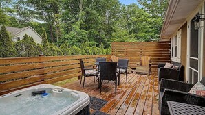 A wooden deck with a hot tub, wicker furniture, and a view of trees.