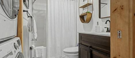 A compact bathroom with a shower curtain, a toilet, a sink with a mirror, and a wooden cabinet.
