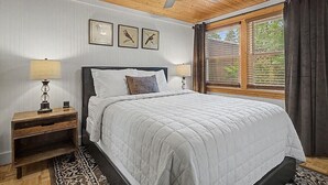 A bedroom with a bed, two bedside tables, a ceiling fan, and three wall-mounted bird paintings.