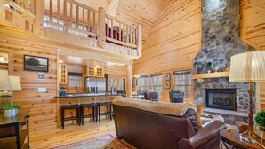 A spacious log cabin interior with a high ceiling, a stone fireplace, a dining area, and a cozy seating area with a leather sofa and a patterned rug. - Timber Nest Goshorn lake dock, pool, town HOT TUB! (Saugatuck)