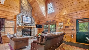 A cozy cabin interior with a stone fireplace, wooden walls, and a large window.