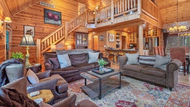 A spacious log cabin interior with a central seating area, a dining table, and a kitchen.