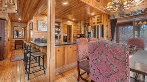 A wooden cabin interior with a kitchen, dining area, and bar.