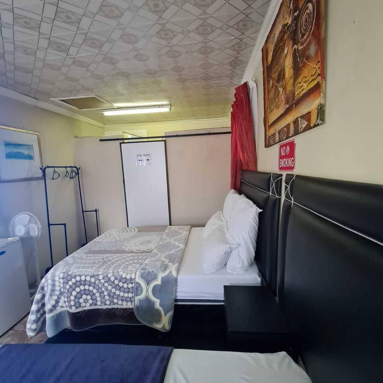 Habitación de hotel con cama, ventilador, armario y cartel de 'No Fumar'.