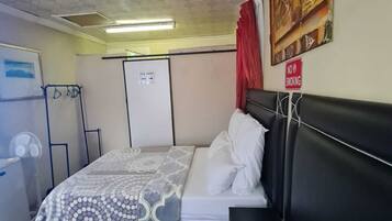 Habitación de hotel con cama, ventilador, armario y cartel de 'No Fumar'.