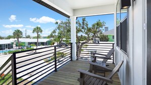 A wooden deck with a railing, a bench, and a view of a street with buildings and a green house. - 🌊Private Pool | Steps to Beach | Ocean Oasis🌊 (Fort Myers Beach)
