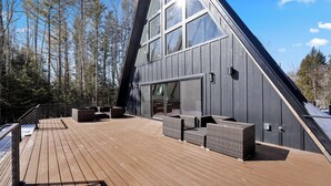 Un edificio moderno con techo inclinado, ventanas amplias y una terraza de madera con mobiliario exterior.