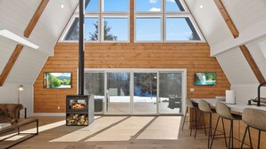 Un loft espacioso con techo alto, paredes de madera, chimenea, un gran ventanal corredero y una zona de bar.