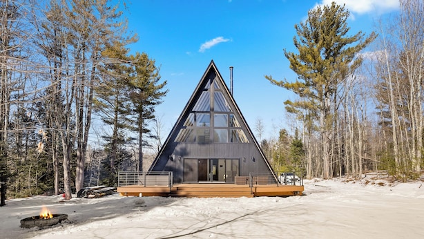 Una cabaña triangular moderna con ventanas amplias, rodeada por un paisaje nevado y altos árboles.
