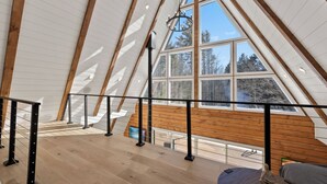 Amplia habitación en el ático con vigas de madera, ventanas grandes y una escalera que sube a un nivel superior.