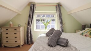 A bedroom with a bed, a dresser, a window with curtains, and a plant. - Figgy Cottage (Ripon)