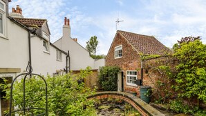 A garden with a brick pathway, a small pond, and lush greenery. - Figgy Cottage (Ripon)