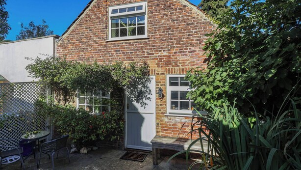 A brick house with a small garden, a wooden bench, and a metal table with chairs. - Figgy Cottage (Ripon)