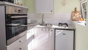 A compact kitchen with a microwave, oven, and refrigerator, a sink, and a window with a view. - Figgy Cottage (Ripon)