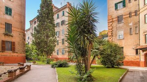 A courtyard with a central palm tree surrounded by greenery, flanked by buildings with brick facades and multiple windows. - KNOWING ROME. (Roma)