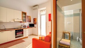 A modern kitchen with a gas stove, microwave, and oven, a small dining area with a red sofa, and a bathroom with a glass shower and toilet. - KNOWING ROME. (Roma)