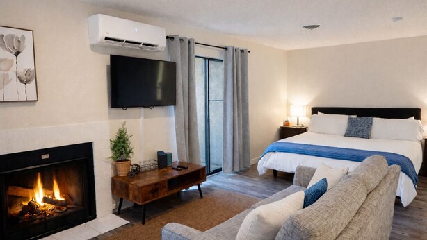 Une chambre d’hôtel avec une cheminée, un téléviseur à écran plat, un lit avec une couverture bleue et un canapé.