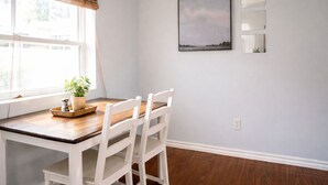 A dining area with a wooden table and white chairs, a potted plant on the windowsill, and a framed picture on the wall. - Beautiful 1 Bdrm • Historical • Downtown (Salt Lake City)