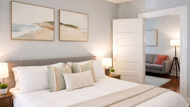 A bedroom with a bed, two bedside tables with lamps, a grey sofa, and a door leading to another room. - Beautiful 1 Bdrm • Historical • Downtown (Salt Lake City)