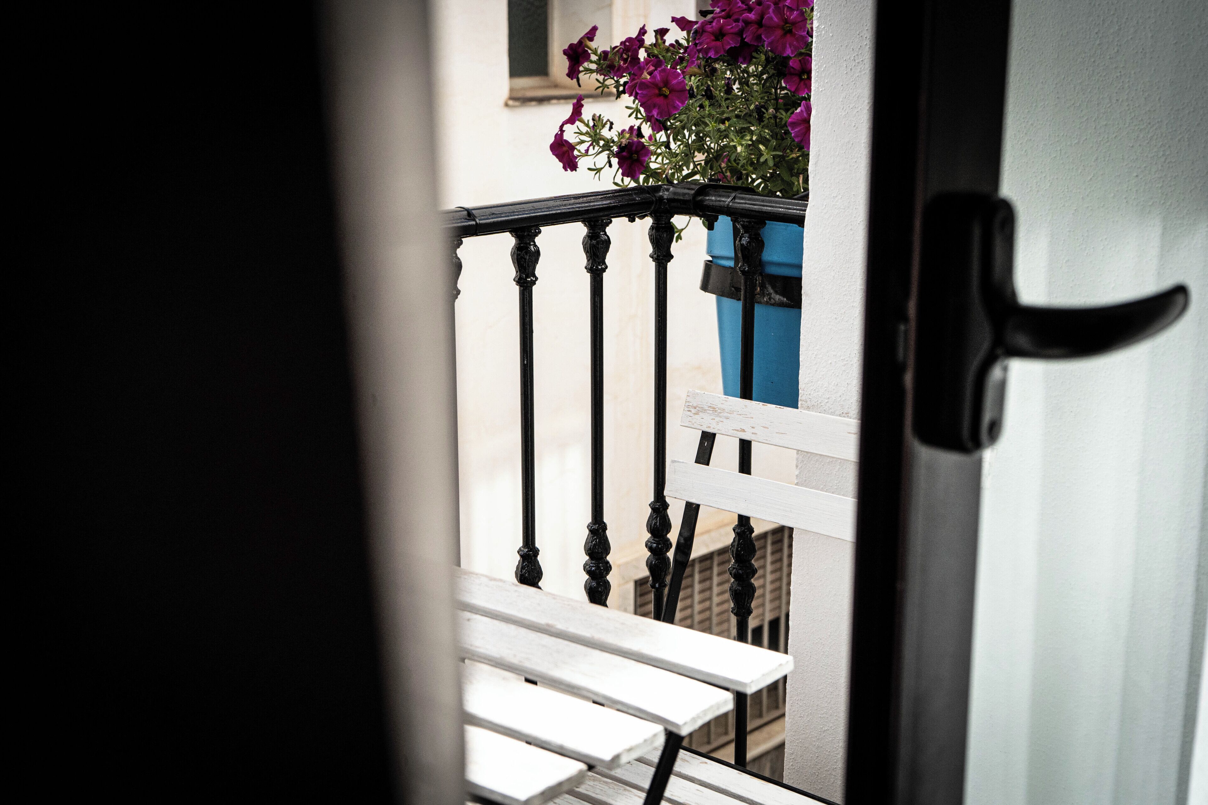 A balcony with a white bench, a blue planter with purple flowers, and a black door handle.