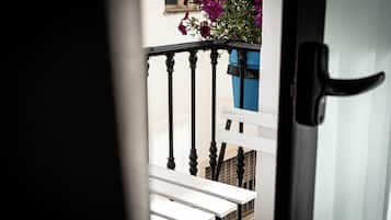 A balcony with a white bench, a blue planter with purple flowers, and a black door handle.