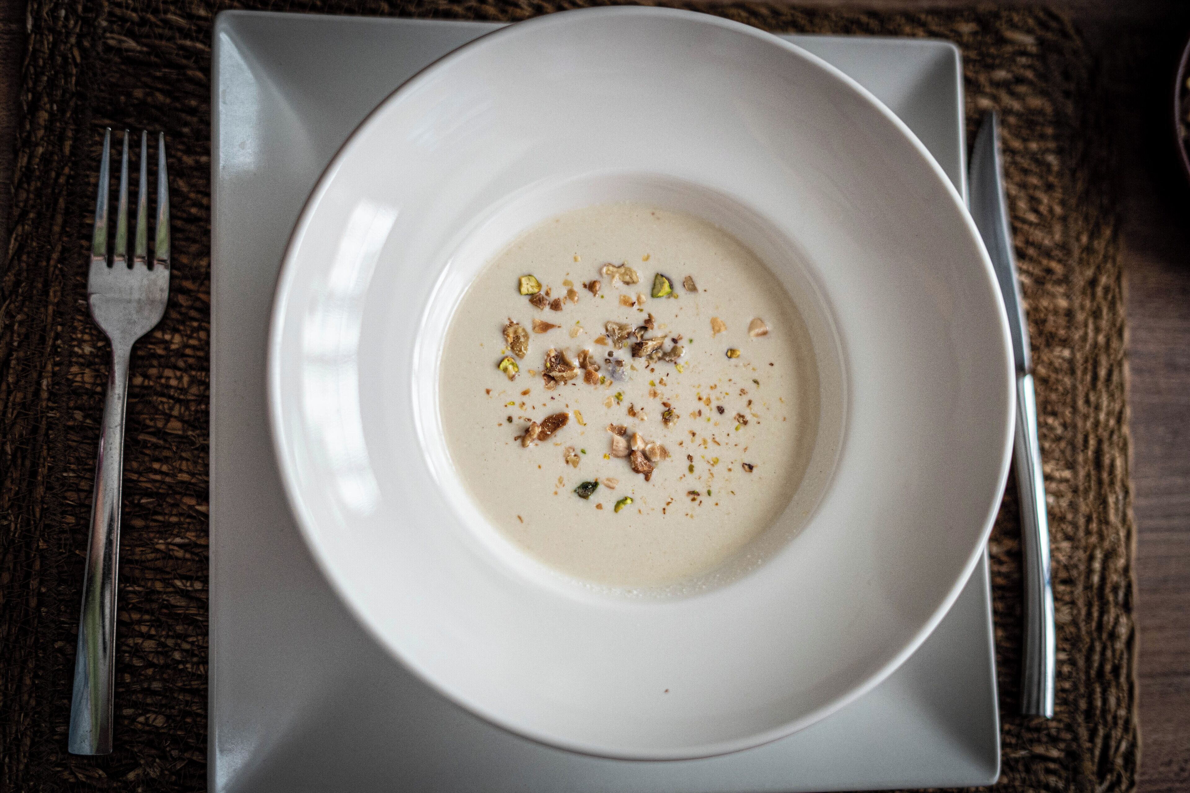 Un bol blanc de sopa sobre un plat blanc, posat sobre un drap de taula quadrat blanc.