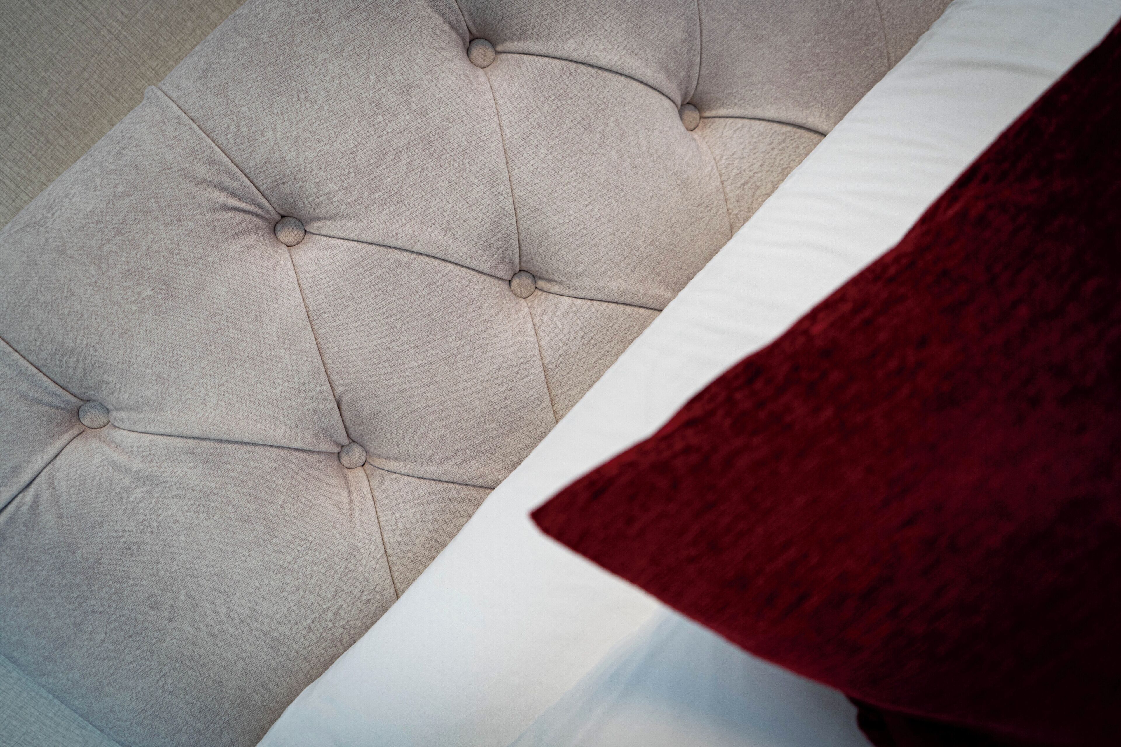 A tufted headboard with a white pillow and a red throw blanket.