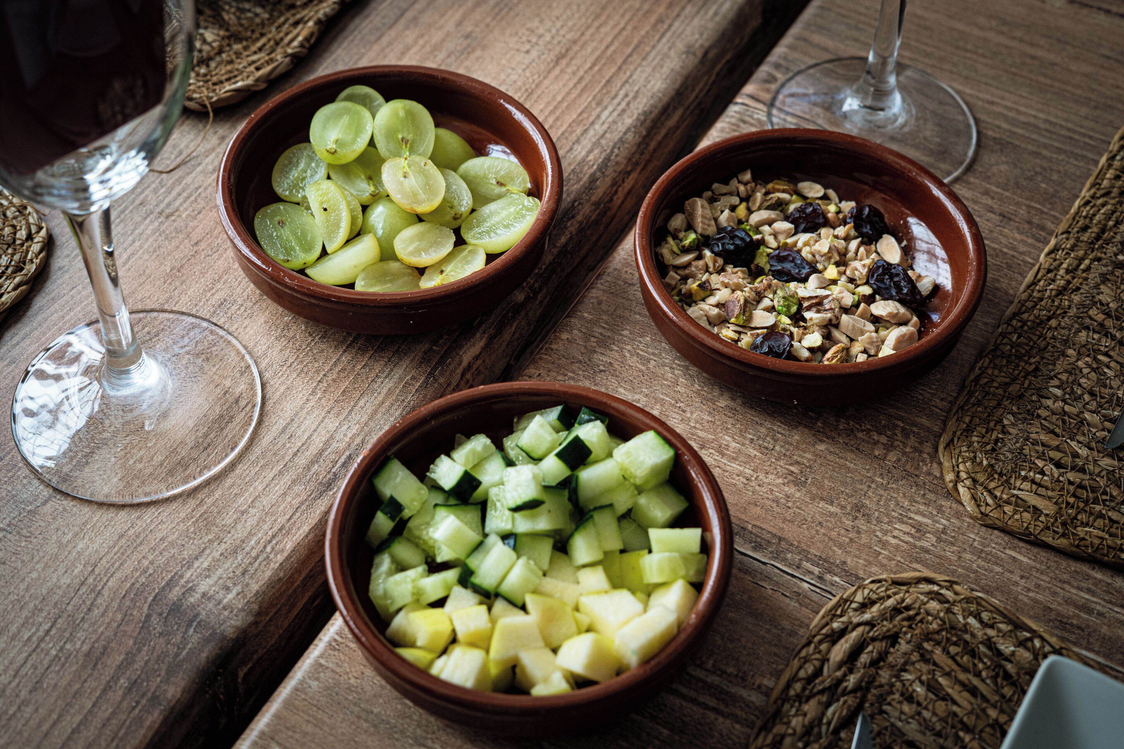 Three bowls of food on a wooden table with two wine glasses.