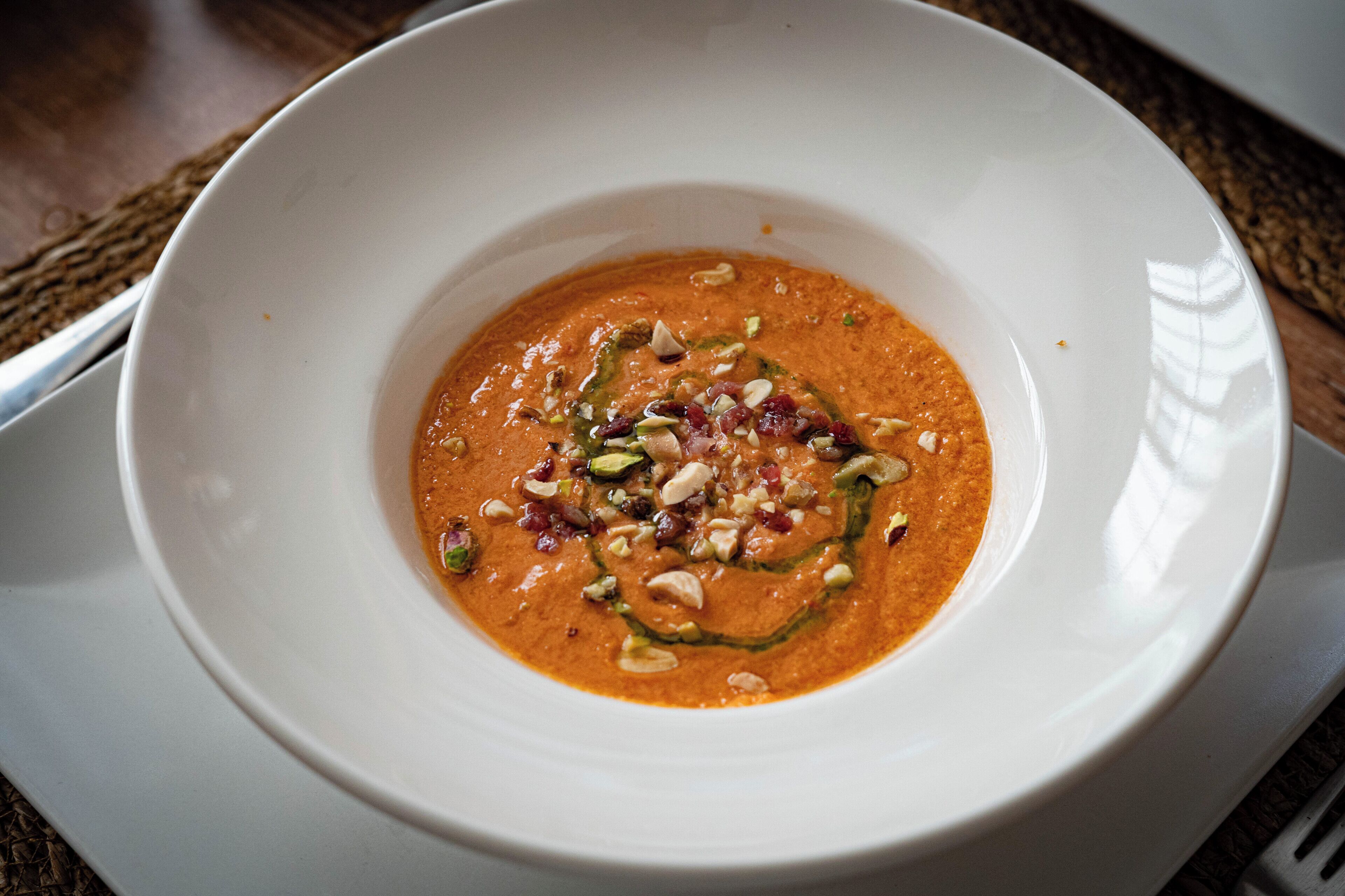 A white bowl of soup with a creamy texture and garnished with nuts and seeds.