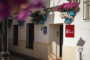 Un bâtiment orné de jardinières suspendues, une enseigne indiquant « Hostal Boutique TOLOX », et une porte marquée de la lettre « H ».