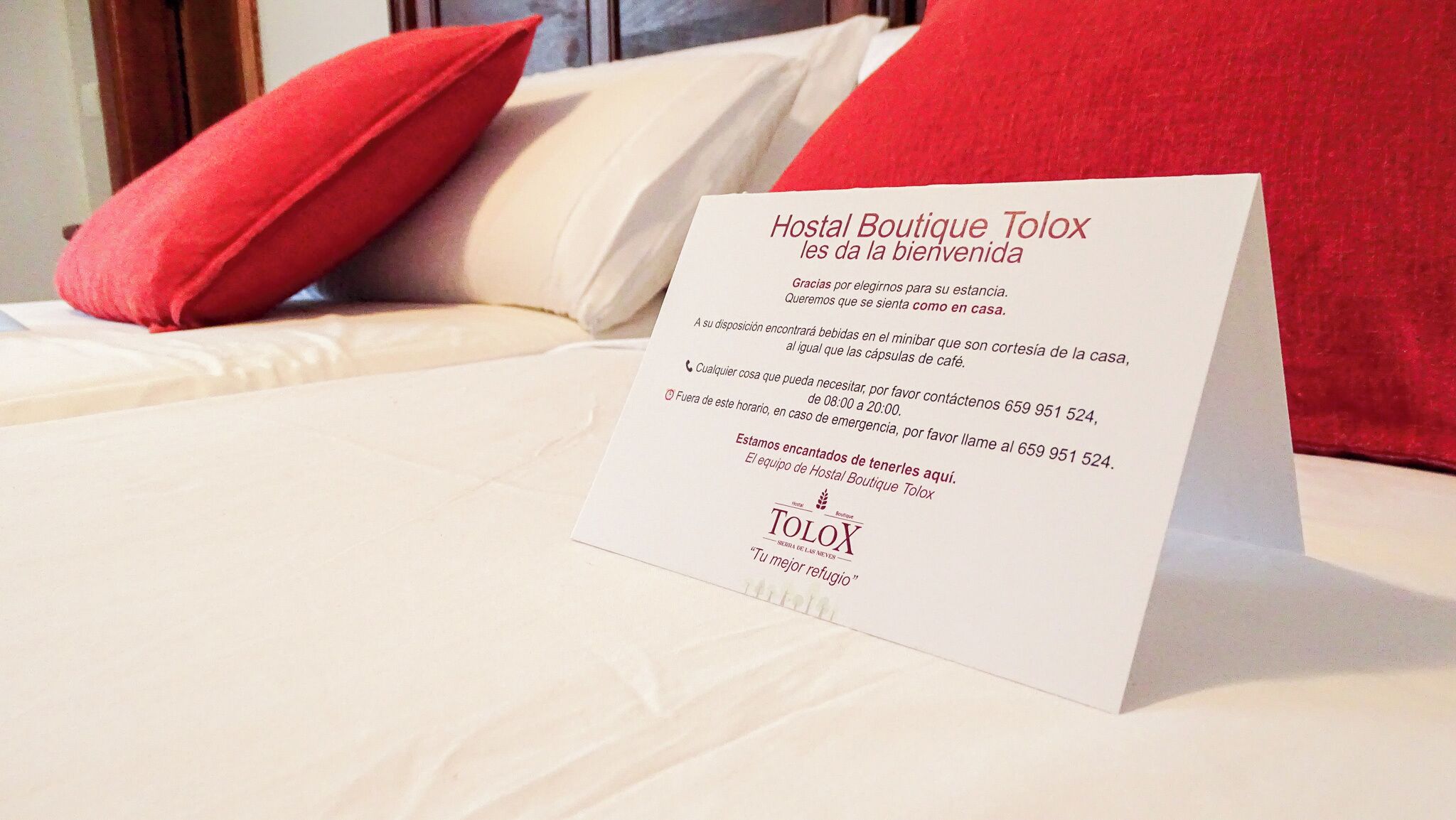 Tarjeta de bienvenida del hotel sobre una cama con almohadas rojas.