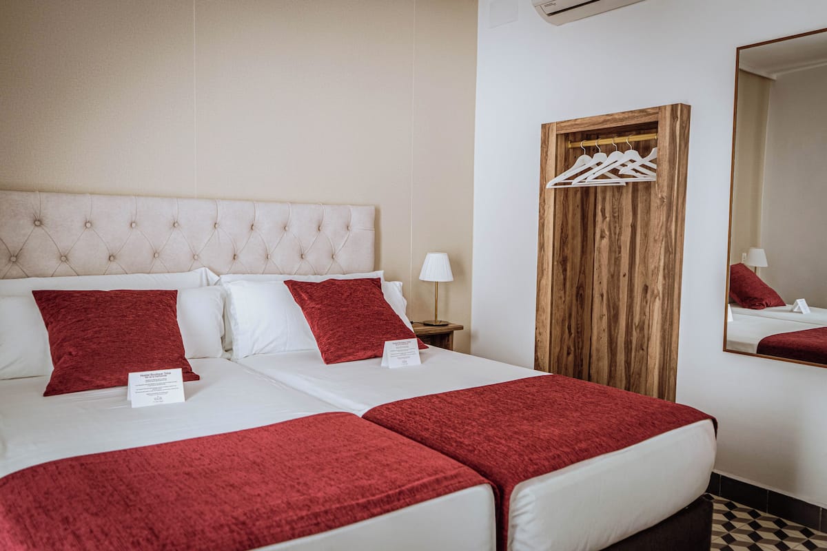 Una habitación de hotel con dos camas, un armario de madera, un espejo y una percha.