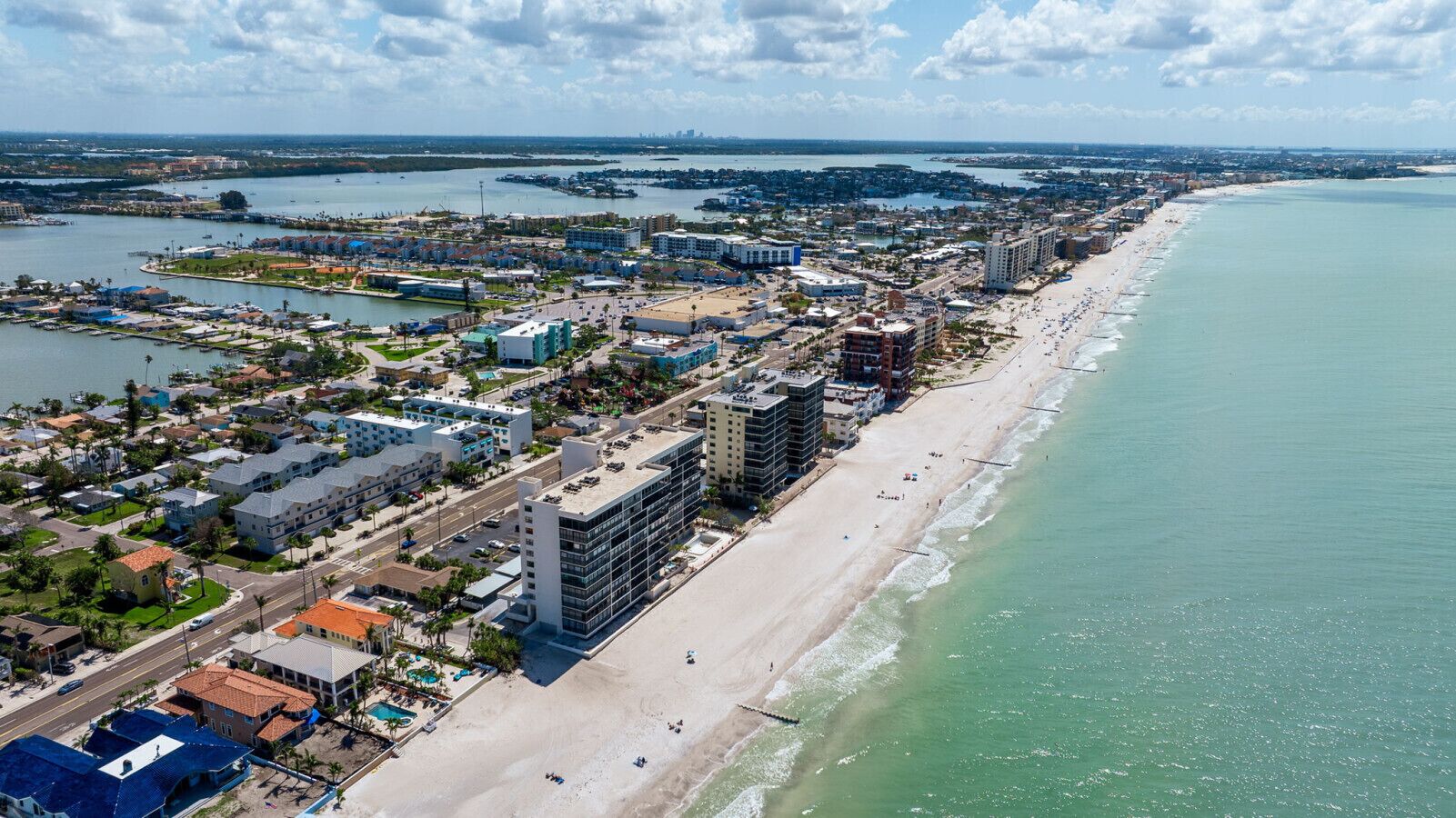 Eine Luftaufnahme einer Küstenstadt mit breitem Strand, dichter Bebauung und einem Yachthafen.