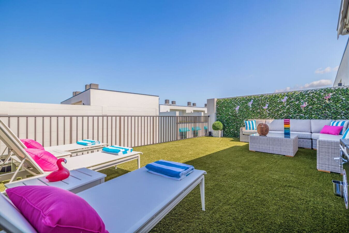 A rooftop terrace with lounge chairs, a sofa, and a green wall with decorative elements.