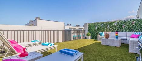 A rooftop terrace with lounge chairs, a sofa, and a green wall with decorative elements.