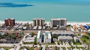 An aerial view of a coastal area with beachfront hotels, a parking lot, and a road leading to the beach.