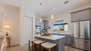 A modern kitchen with a large island, bar stools, stainless steel appliances, and a view of the beach.