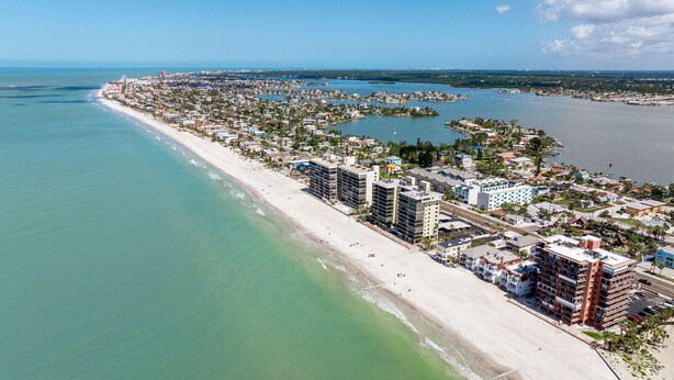 An aerial view of a coastal area with a beach, buildings, and water bodies.