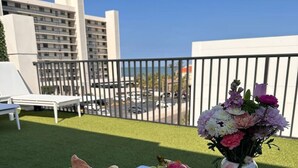 A balcony with a table set for breakfast, including croissants, fruit, and coffee, with a city view in the background.