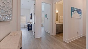 A hallway with a wooden floor, a bench, a table, and a painting on the wall.