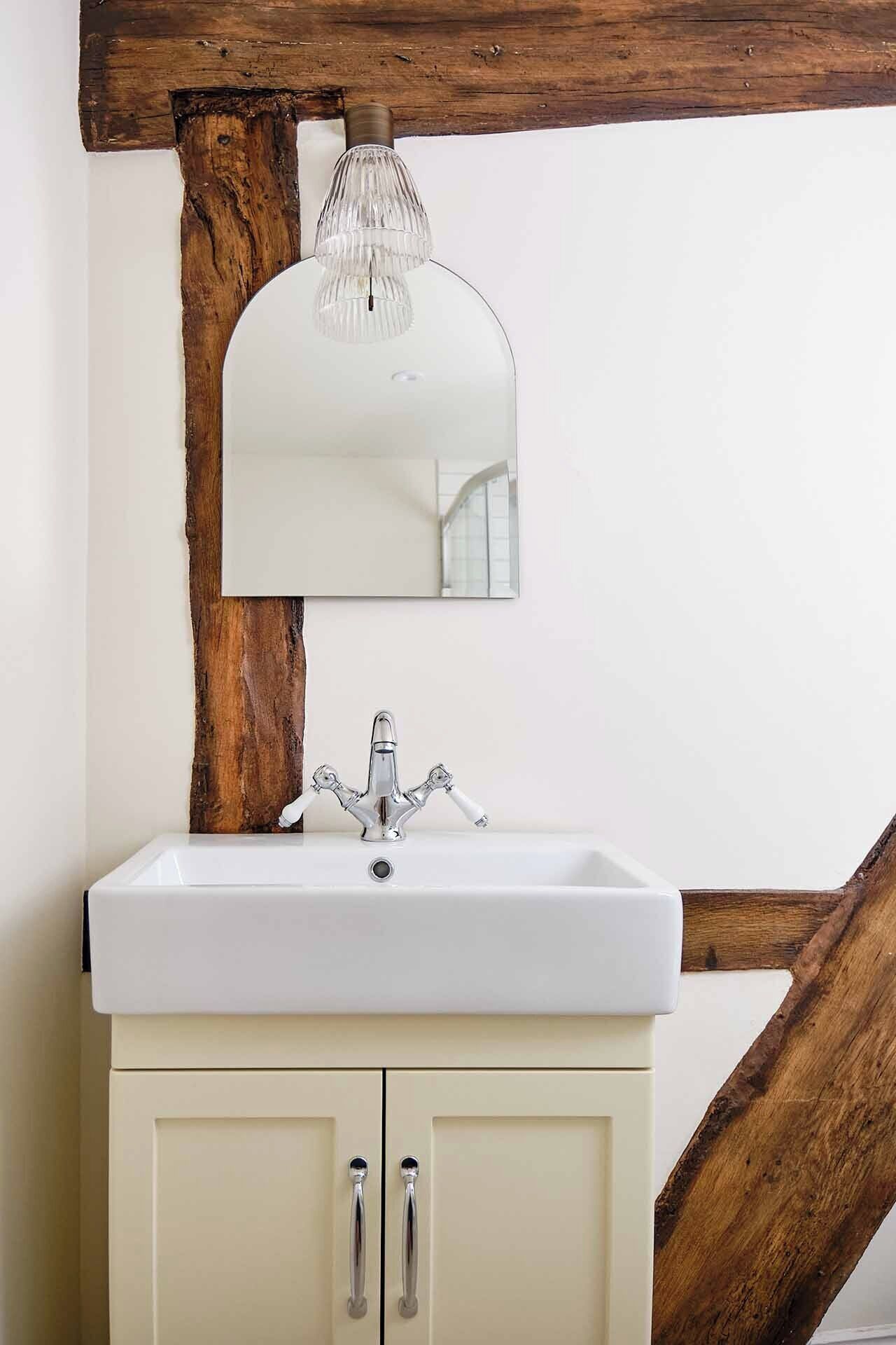 Un baño con un lavabo blanco, un espejo y una viga de madera arriba.