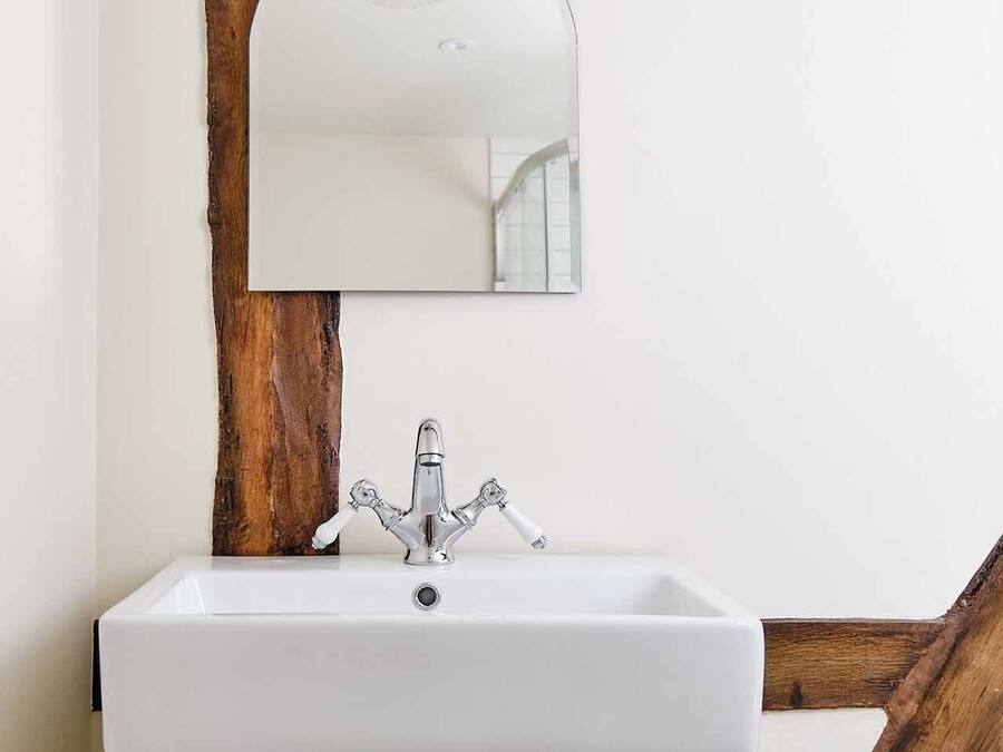 Un baño con un lavabo blanco, un espejo y una viga de madera arriba.